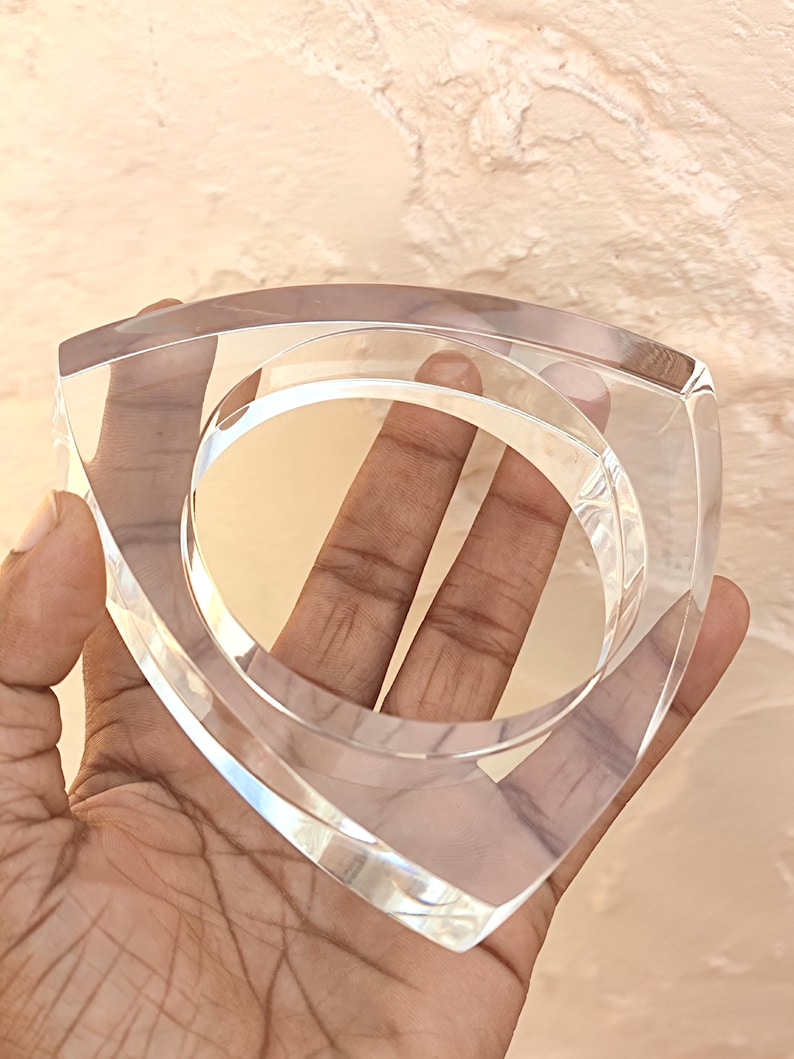 Op de afbeelding: Een heldere, vierkante acrylarmband met afgeronde binnenranden. De armband heeft een transparante uitstraling, waardoor licht erdoorheen kan schijnen. Het ontwerp is modern en minimalistisch, geschikt voor diverse stijlen.