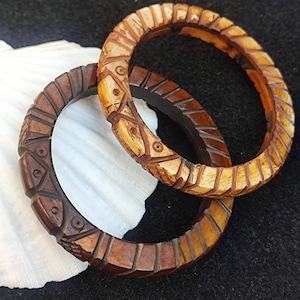 May include: Two intricately carved wooden bangles, one brown and one light brown with a geometric pattern.