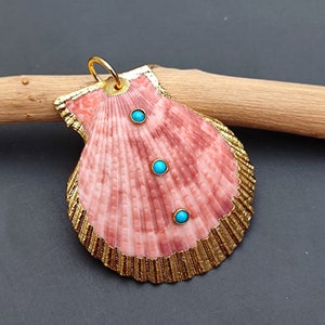 K&ouml;nnte beinhalten: Ein rosa Muschel-Anh&auml;nger mit goldener Umrandung und drei t&uuml;rkisfarbenen Steinen. Der Anh&auml;nger h&auml;ngt an einer goldenen Kette.