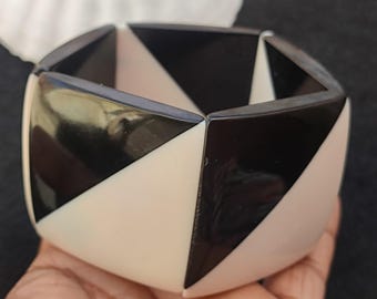 May include: A black and white geometric bracelet made of plastic. The bracelet is made up of triangular shapes that alternate in colour.