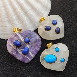 May include: Three heart-shaped pendants with gold accents and oval-shaped gemstones. The pendants are made of clear quartz and amethyst. One pendant has three blue gemstones, one has three turquoise gemstones, and one has three blue gemstones.