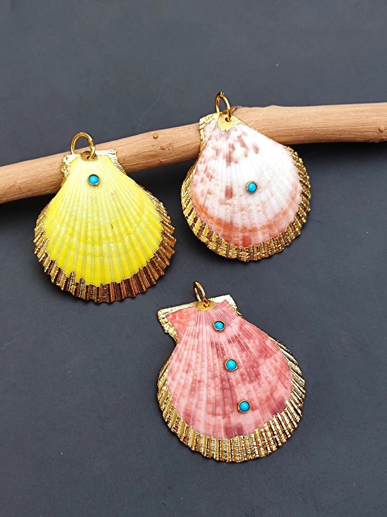 K&ouml;nnte beinhalten: Drei goldger&auml;nderte Muscheln mit t&uuml;rkisfarbenen Akzenten. Die Muscheln sind gelb, rosa und wei&szlig; mit einer nat&uuml;rlichen, strukturierten Oberfl&auml;che.