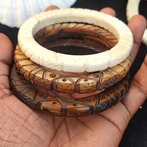 May include: Three intricately carved bangles, one white and two brown, with geometric patterns and small holes. The bangles are stacked on top of each other.