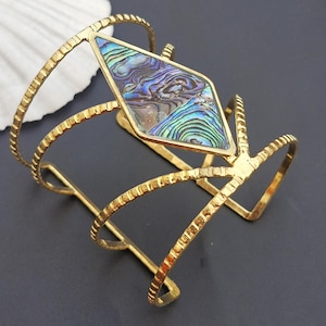 May include: Gold-toned metal cuff bracelet with a diamond-shaped abalone shell inlay. The bracelet has a textured, patterned design.
