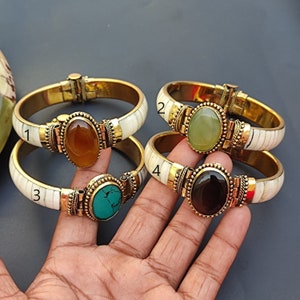 Peut inclure: Quatre bracelets en or avec des incrustations d'os blancs et des accents de pierres précieuses de différentes couleurs. Les bracelets sont empilés les uns sur les autres. Les pierres précieuses sont l'ambre, le vert, la turquoise et le noir.