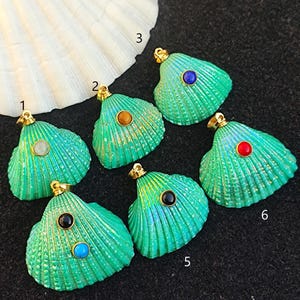 May include: Six green seashell pendants with different coloured gemstones in the centre. The seashells are iridescent and have a gold accent.