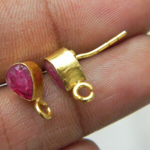 Pu&ograve; includere: Un paio di orecchini d'oro con accenti di pietre preziose rosa. Gli orecchini hanno un design semplice con una piccola pietra preziosa a forma di lacrima incastonata in una montatura d'oro. Gli orecchini sono attaccati a un perno d'oro con un piccolo anello all'estremit&agrave;.