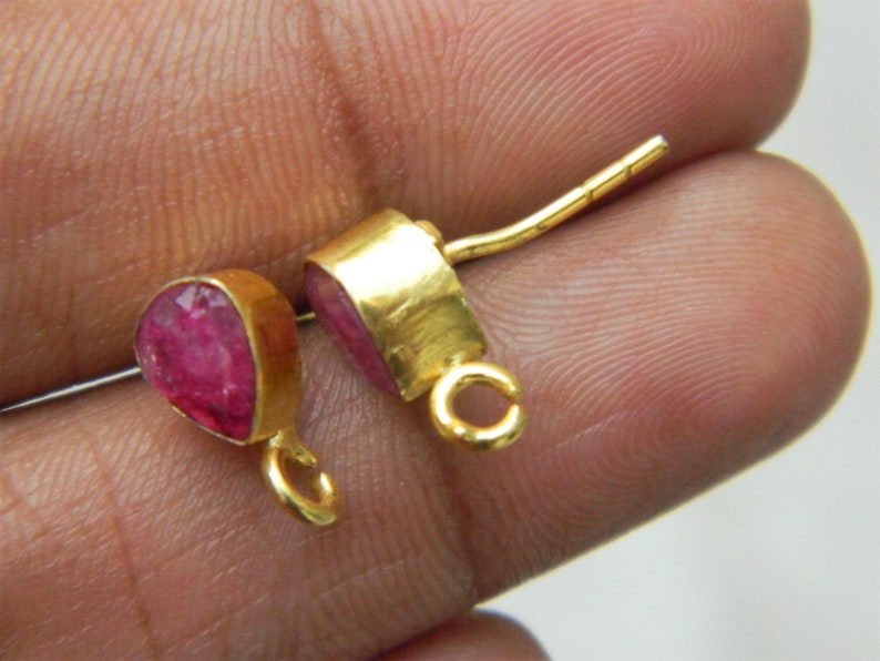 Pu&ograve; includere: Un paio di orecchini d'oro con accenti di pietre preziose rosa. Gli orecchini hanno un design semplice con una piccola pietra preziosa a forma di lacrima incastonata in una montatura d'oro. Gli orecchini sono attaccati a un perno d'oro con un piccolo anello all'estremit&agrave;.