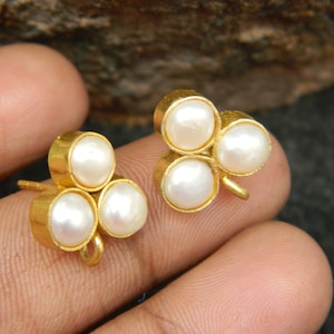 May include: A pair of gold-tone earrings with three white pearl accents each. The earrings have a clover-shaped design.