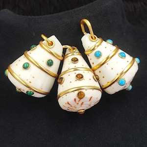 Pode incluir: Três pingentes em forma de concha com detalhes em metal dourado. Cada pingente é adornado com pequenas pedras preciosas coloridas: verde, marrom e azul. Os pingentes têm uma argola na parte superior para pendurar.