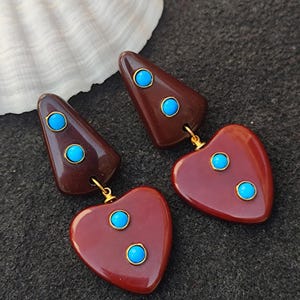 May include: A pair of dangle earrings with a brown heart and triangle shape. Each earring has three turquoise blue stones.