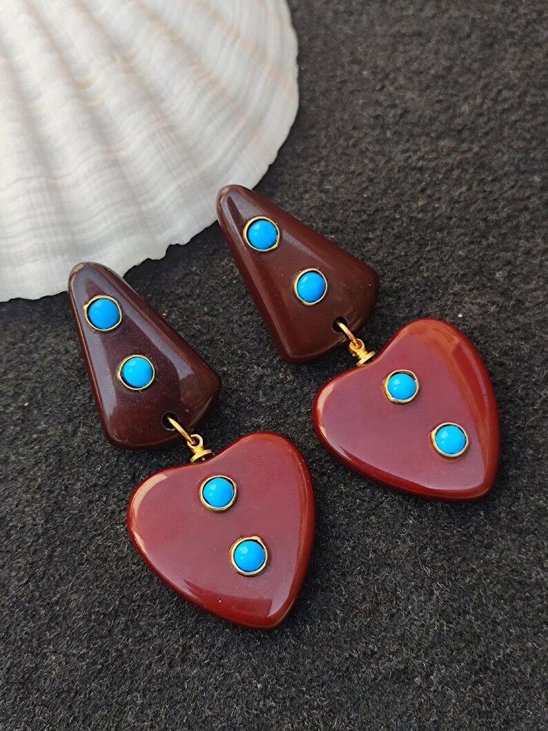 May include: A pair of dangle earrings with a brown heart and triangle shape. Each earring has three turquoise blue stones.