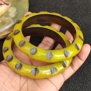 May include: Two yellow bangles with black and grey patterned accents. The bangles are stacked on top of each other.