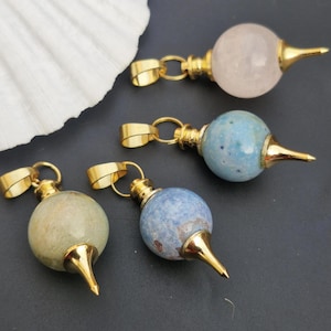 Puede incluir: Cuatro colgantes de tono dorado con orbes de piedras preciosas de diferentes colores y puntas puntiagudas. Los orbes son rosados, azules, verdes y azules con motas blancas.