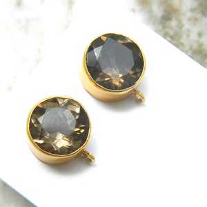 May include: Two gold-toned round pendant charms with a clear smoky quartz gemstone in the center. Each charm has a small loop on the side.