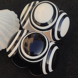 Può includere: Un set di quattro braccialetti rotondi a righe bianche e nere. I braccialetti sono realizzati in materiale lucido e hanno un design semplice.