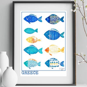May include: Framed art print with nine patterned fish illustrations in blue, yellow, and orange. The word "GREECE" is printed in blue at the bottom. The artwork is displayed on a white surface. The print is in a black frame.