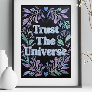 May include: A black and white print with the text "Trust The Universe" in a blue and purple font. The text is surrounded by a floral design in shades of purple, blue, and green.
