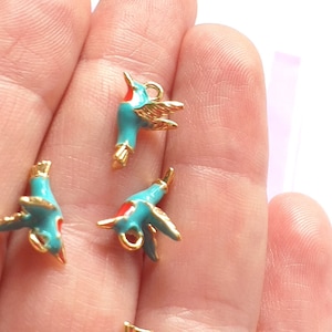 Può includere: Piccoli ciondoli a forma di colibrì turchese e dorati. I ciondoli hanno accenti rossi sul becco e sulla testa. I ciondoli sono in metallo e hanno un anello per attaccarli a gioielli o altri lavori artigianali.