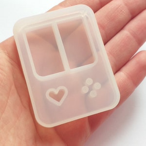 May include: Clear silicone mold shaped like a handheld video game console with two rectangular spaces for resin, a heart-shaped button, and four round buttons.