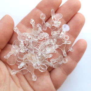 May include: A pile of clear plastic ear nuts for glasses, held in a hand.