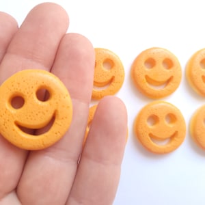 Peut inclure: Gros plan sur une main tenant un bouton jaune en forme de smiley. Il y a plusieurs autres boutons jaunes en forme de smiley en arrière-plan.