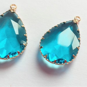 May include: Two teardrop-shaped turquoise blue glass pendants with gold-toned metal settings. The pendants have a faceted design and are ideal for jewellery making.
