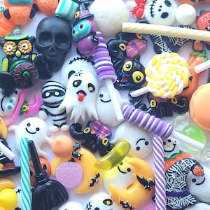 Peut inclure: Assortiment de breloques et de décorations de bonbons sur le thème d'Halloween. Les breloques sont en résine et présentent divers motifs effrayants, notamment des fantômes, des citrouilles, des chauves-souris et des crânes. Les décorations de bonbons sont en plastique et présentent divers motifs de bonbons, notamment des sucettes, des cannes en sucre et des barres chocolatées.