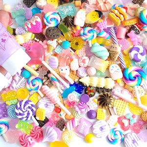 May include: A selection of colourful miniature candy and sweets, including lollipops, gummies and chocolate bars, are scattered on a white surface. Three tubes of colourful slime are also visible in the image. The tubes are labelled with the text "仿真奶油 Simulation Cream 50g".