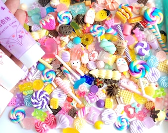 May include: A variety of colorful miniature candy and sweets, including lollipops, gummies, and chocolate bars, are scattered on a white surface. Three tubes of colorful slime are also visible in the image. The tubes are labeled with the text "仿真奶油 Simulation Cream 50g".