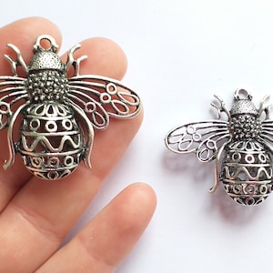 May include: Two silver bee charms with intricate details and openwork wings. The bees have a patterned body and a loop for attaching to jewelry or crafts.