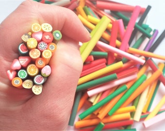 Op de afbeelding: Een verzameling kleurrijke polymer clay-staven met verschillende fruitontwerpen, waaronder watermeloen, aardbei, kiwi en sinaasappelschijfjes. De staven zijn in een hand gerangschikt, met een grotere stapel geassorteerde gekleurde staven op de achtergrond.
