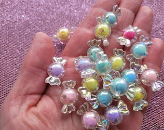 May include: A collection of iridescent candy-shaped charms in various pastel colors, including pink, blue, yellow, and purple. The charms are made of clear plastic with a holographic finish.