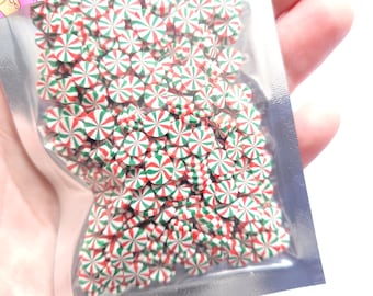 Op de afbeelding: Een close-up van een zak gevuld met rode en groene pepermuntsprinkels. De sprinkels zijn klein en rond, met een witte achtergrond en rode en groene strepen.