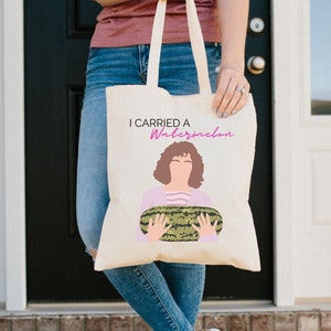 May include: A white canvas tote bag with a pink and green illustration of a woman holding a watermelon. The text "I carried a watermelon" is printed on the bag in pink.