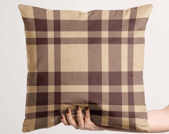 May include: A brown and beige plaid throw pillow with a subtle pattern. The pillow is being held by a hand.