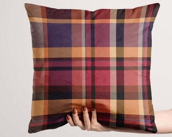 May include: A red, brown, and black plaid throw pillow with a subtle sheen. The pillow is being held by a hand.
