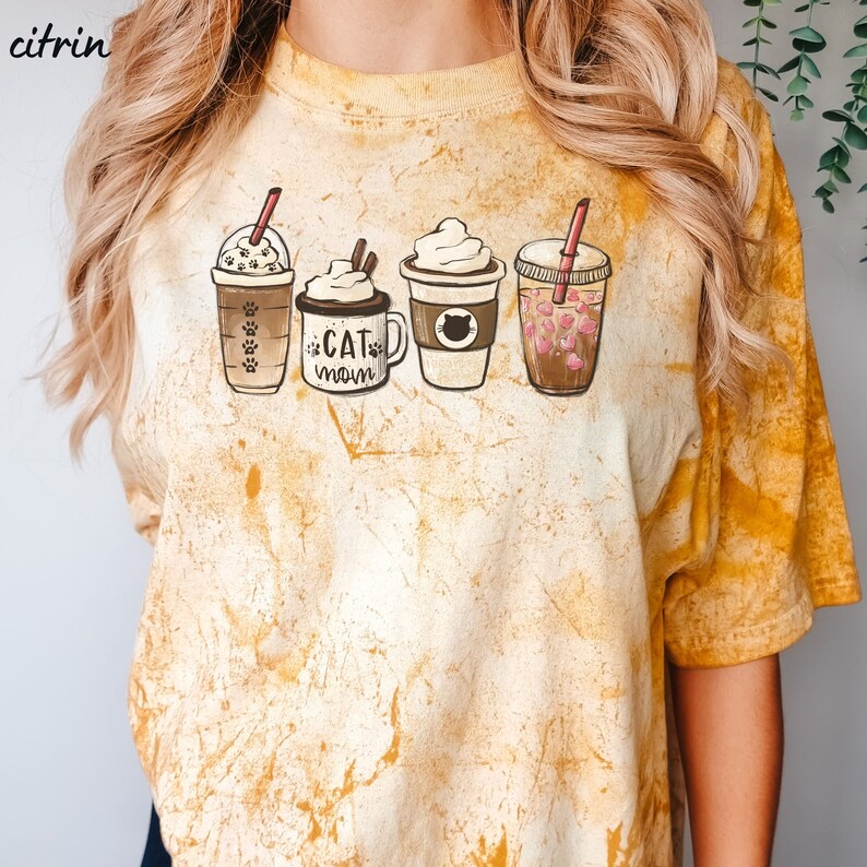 May include: A yellow tie-dye t-shirt with a graphic of four different coffee drinks. The text "Cat Mom" is on one of the coffee cups.