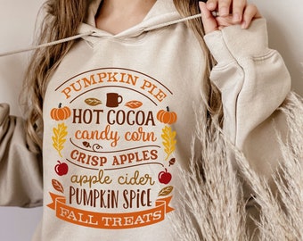 May include: Beige hoodie with a fall-themed graphic. The design includes the words "Pumpkin Pie, Hot Cocoa, Candy Corn, Crisp Apples, Apple Cider, Pumpkin Spice, Fall Treats" with illustrations of pumpkins, leaves, and apples.