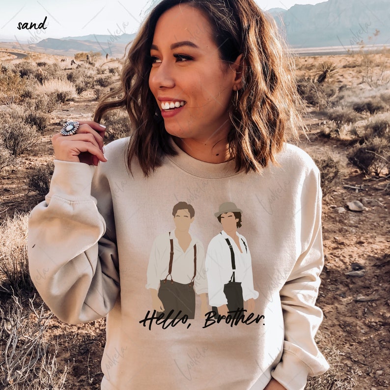 May include: A beige sweatshirt featuring a graphic print of two men in suspenders and hats. The text "Hello, Brother." is printed beneath the graphic.