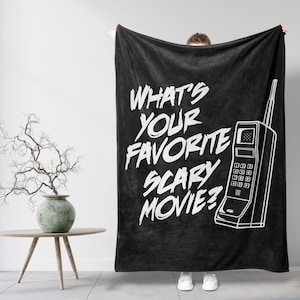 Può includere: Coperta in pile nera con testo bianco che recita "Qual è il tuo film horror preferito?" e un contorno bianco di un telefono rotatorio vintage.