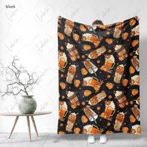Op de afbeelding: Een zwarte fleece deken met een herhalend patroon van oranje pompoenen, koffiebekers en bierglazen. Het patroon is op een zwarte achtergrond met witte sterren.