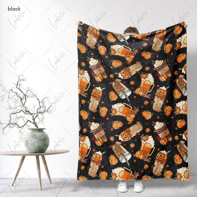 Op de afbeelding: Een zwarte fleece deken met een herhalend patroon van oranje pompoenen, koffiebekers en bierglazen. Het patroon is op een zwarte achtergrond met witte sterren.