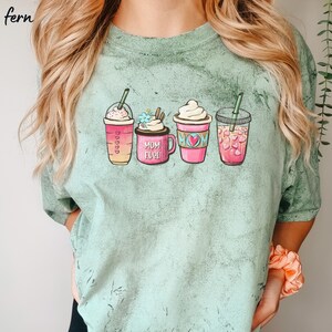 Puede incluir: Una camiseta verde claro con un gr&aacute;fico de cuatro bebidas de caf&eacute; diferentes. Las bebidas est&aacute;n etiquetadas como "Mom Fuel" y tienen corazones y flores.