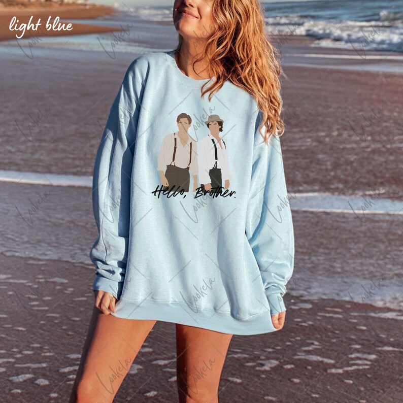 May include: A light blue sweatshirt featuring a graphic print of two men standing side-by-side. The text "Hello, Brother." is printed below the graphic.