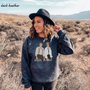 May include: A dark heather grey sweatshirt with a graphic print of two men standing side-by-side. The text "Hello, Brother" is printed below the graphic.