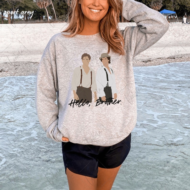 May include: A grey sweatshirt featuring a graphic of two men standing side-by-side. The text "Hello, Brother." is printed below the graphic.