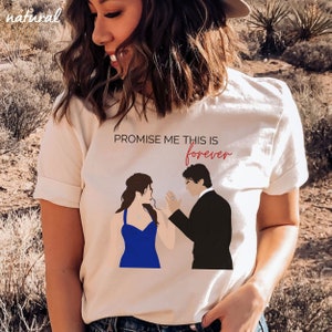 May include: A cream-colored t-shirt featuring the text "PROMISE ME THIS IS forever" in black and red. The shirt has a graphic of a man in a black suit proposing to a woman in a blue dress. The word "natural" is in the top left corner.
