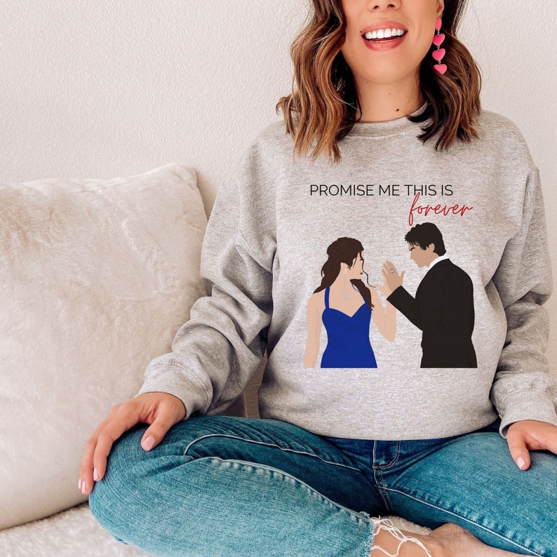 May include: A gray sweatshirt with a graphic print of a couple in a romantic pose. The text "PROMISE ME THIS IS forever" is printed on the sweatshirt.