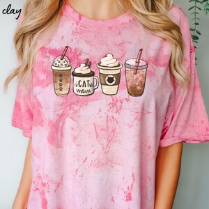 May include: Pink tie-dye t-shirt with a graphic of four different coffee drinks. The coffee drinks are labeled "Cat Mom".